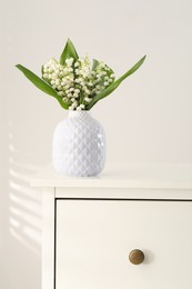 Photo of Beautiful lilies of the valley flowers in vase on chest of drawers
