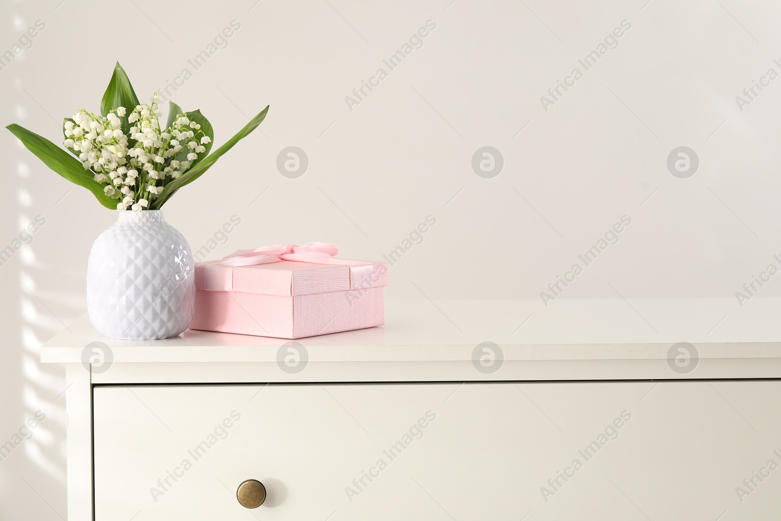 Beautiful lilies of the valley flowers and gift on white table. Space for text Photo of Beautiful lilies of the valley flowers and gift on white table. Space for text