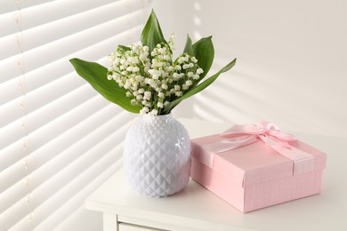 Photo of Beautiful lilies of the valley flowers and gift on white table indoors