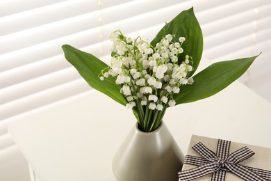 Photo of Beautiful lilies of the valley flowers and gift on table indoors, closeup