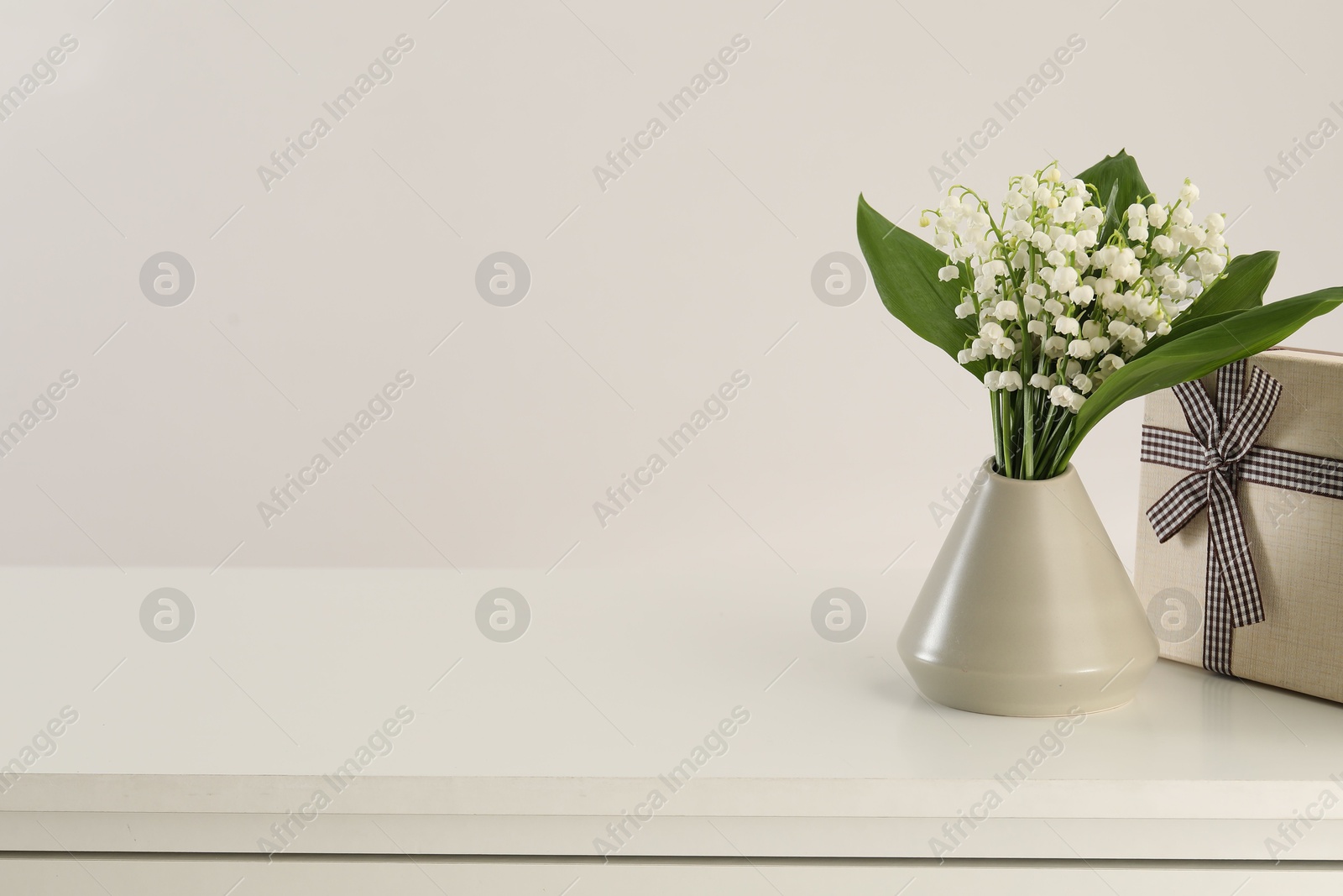 Beautiful lilies of the valley flowers and gift on white table. Space for text Photo of Beautiful lilies of the valley flowers and gift on white table. Space for text