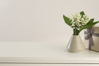 Photo of Beautiful lilies of the valley flowers and gift on white table. Space for text