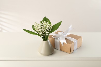 Photo of Beautiful lilies of the valley flowers and gift on white table