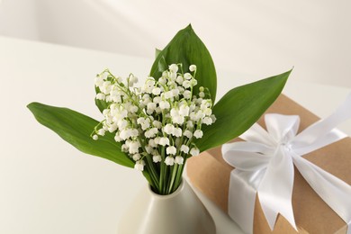 Photo of Beautiful lilies of the valley flowers and gift on white table, closeup