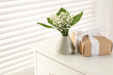 Photo of Beautiful lilies of the valley flowers and gift on white table indoors. Space for text