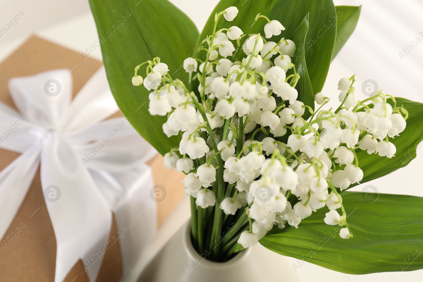 Beautiful lilies of the valley flowers and gift on white table, closeup Photo of Beautiful lilies of the valley flowers and gift on white table, closeup