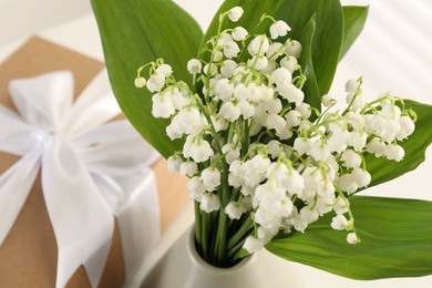 Photo of Beautiful lilies of the valley flowers and gift on white table, closeup