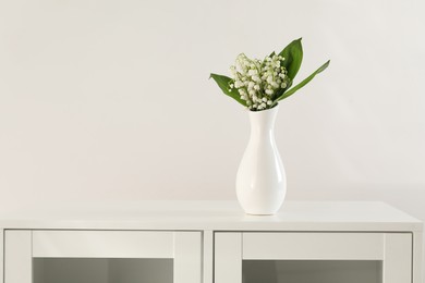 Photo of Beautiful lilies of the valley flowers in vase on cabinet. Space for text