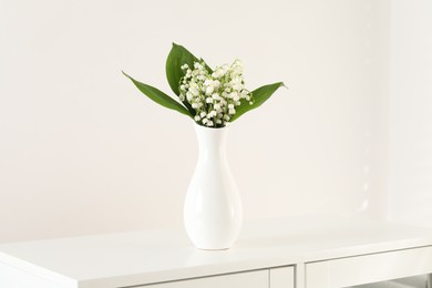 Photo of Beautiful lilies of the valley flowers in vase on cabinet