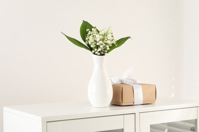 Photo of Beautiful lilies of the valley flowers and gift on white cabinet