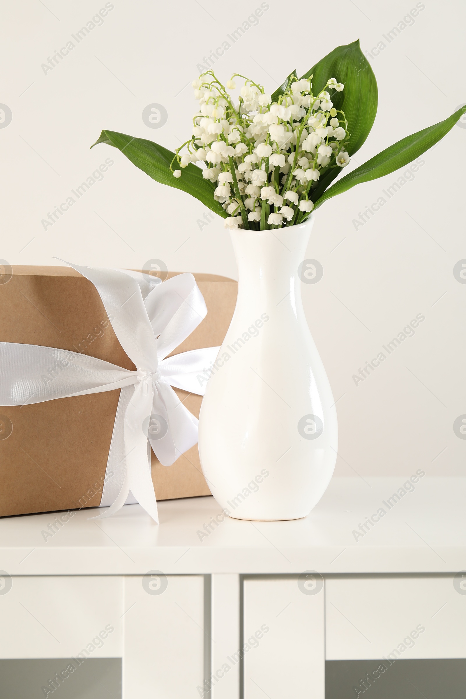 Beautiful lilies of the valley flowers and gift on white cabinet Photo of Beautiful lilies of the valley flowers and gift on white cabinet