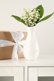 Photo of Beautiful lilies of the valley flowers and gift on white cabinet