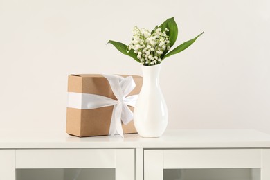 Photo of Beautiful lilies of the valley flowers and gift on white cabinet