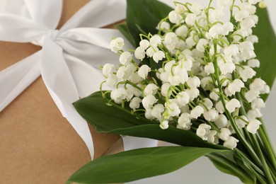 Photo of Beautiful lilies of the valley flowers and gift on white table, closeup
