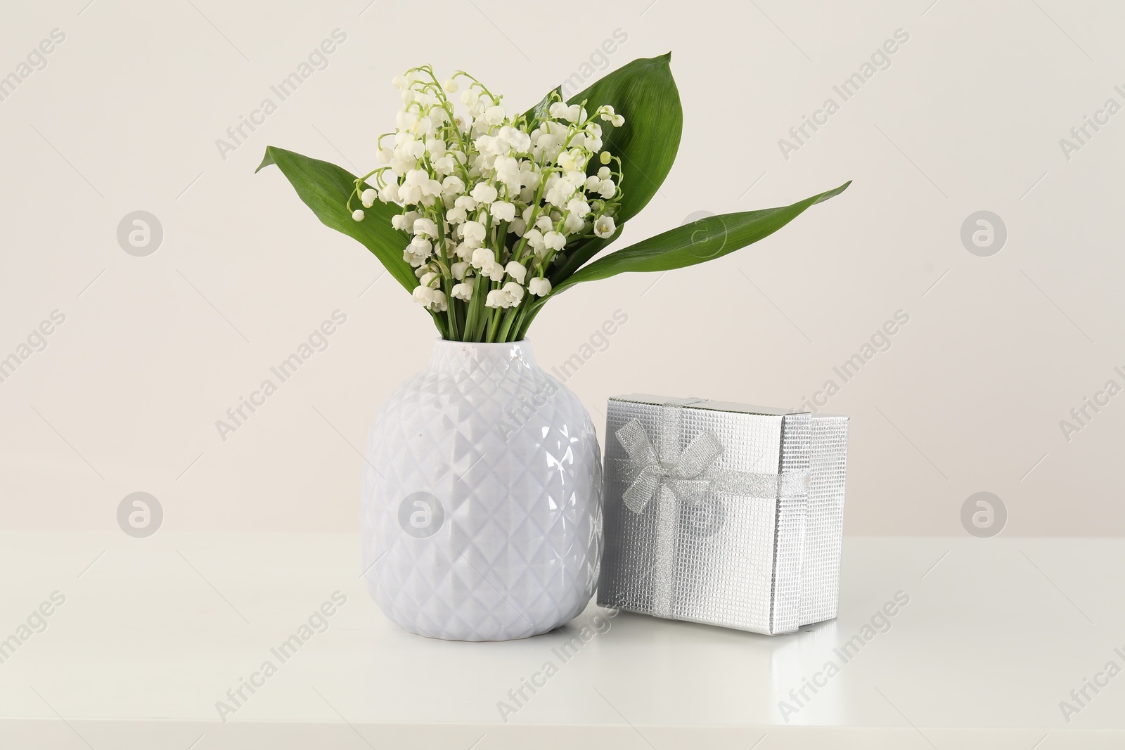 Beautiful lilies of the valley flowers and gift on white table Photo of Beautiful lilies of the valley flowers and gift on white table