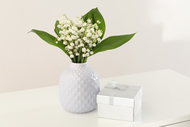 Photo of Beautiful lilies of the valley flowers and gift on white table