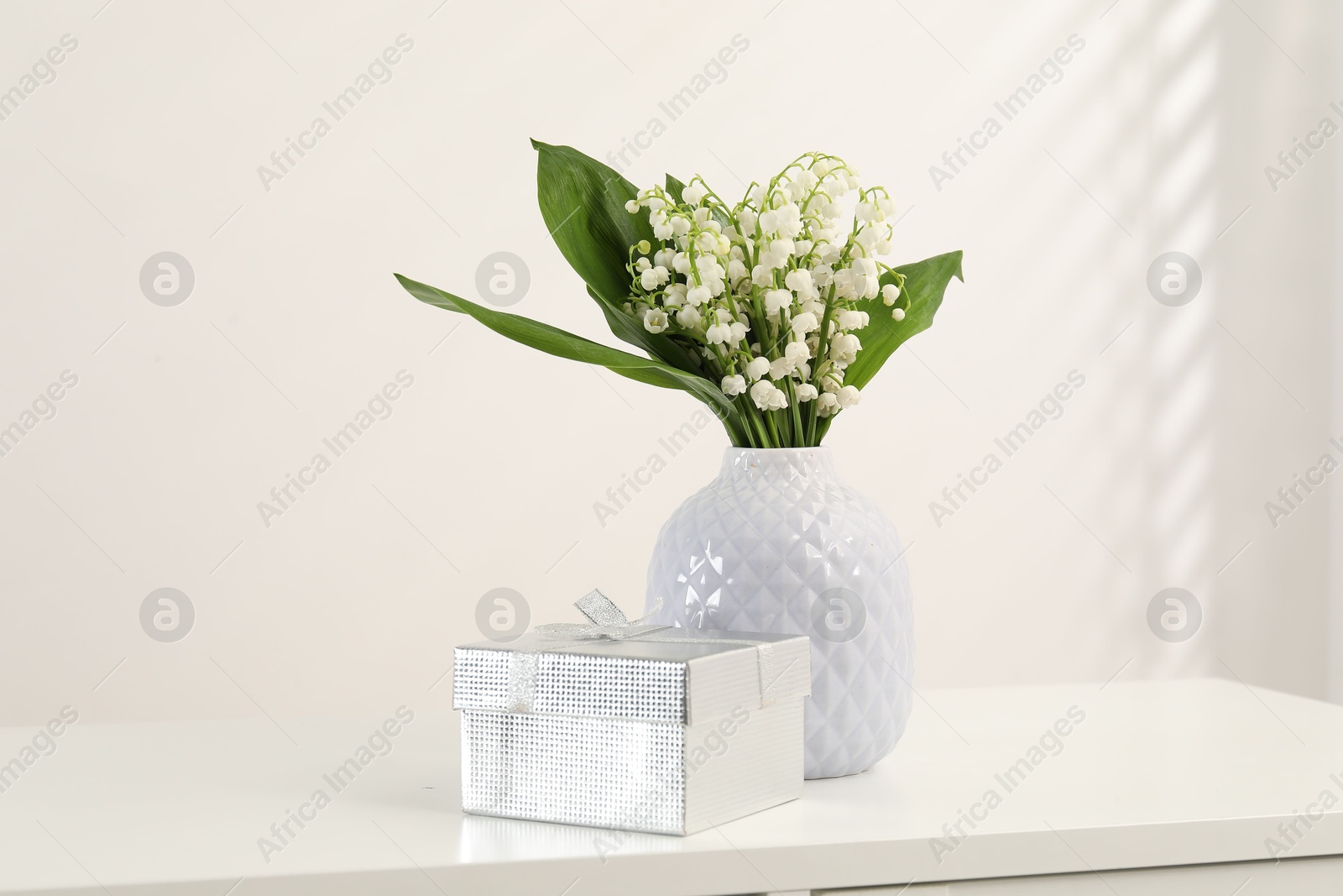 Beautiful lilies of the valley flowers and gift on white table Photo of Beautiful lilies of the valley flowers and gift on white table