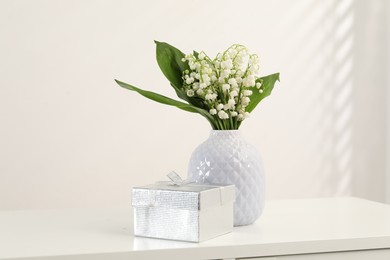 Photo of Beautiful lilies of the valley flowers and gift on white table