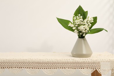 Photo of Beautiful lilies of the valley flowers in vase on table. Space for text