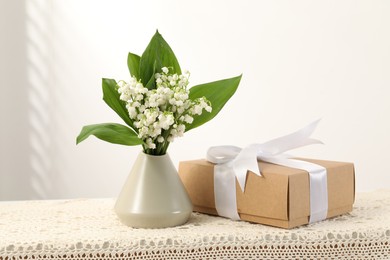 Photo of Beautiful lilies of the valley flowers and gift on table