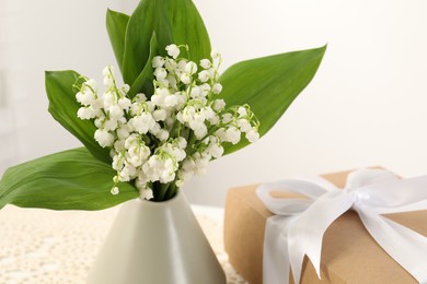 Photo of Beautiful lilies of the valley flowers and gift on table, closeup