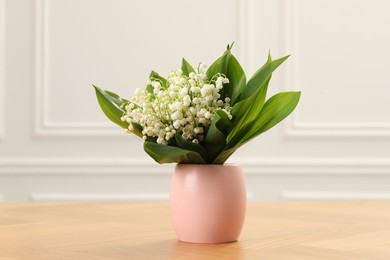 Photo of Beautiful lilies of the valley flowers in vase on wooden table