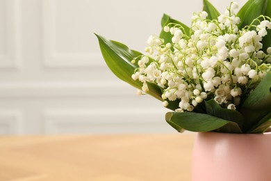 Photo of Beautiful lilies of the valley flowers in vase on wooden table, closeup. Space for text