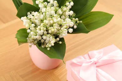 Photo of Beautiful lilies of the valley flowers and gift on wooden table, closeup