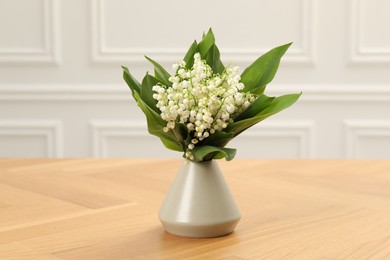 Photo of Beautiful lilies of the valley flowers in vase on wooden table
