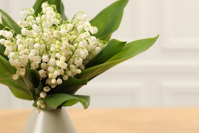 Photo of Beautiful lilies of the valley flowers in vase on wooden table, closeup
