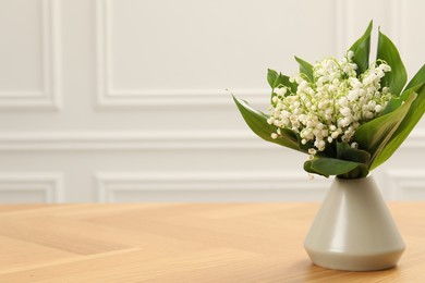 Photo of Beautiful lilies of the valley flowers in vase on wooden table. Space for text