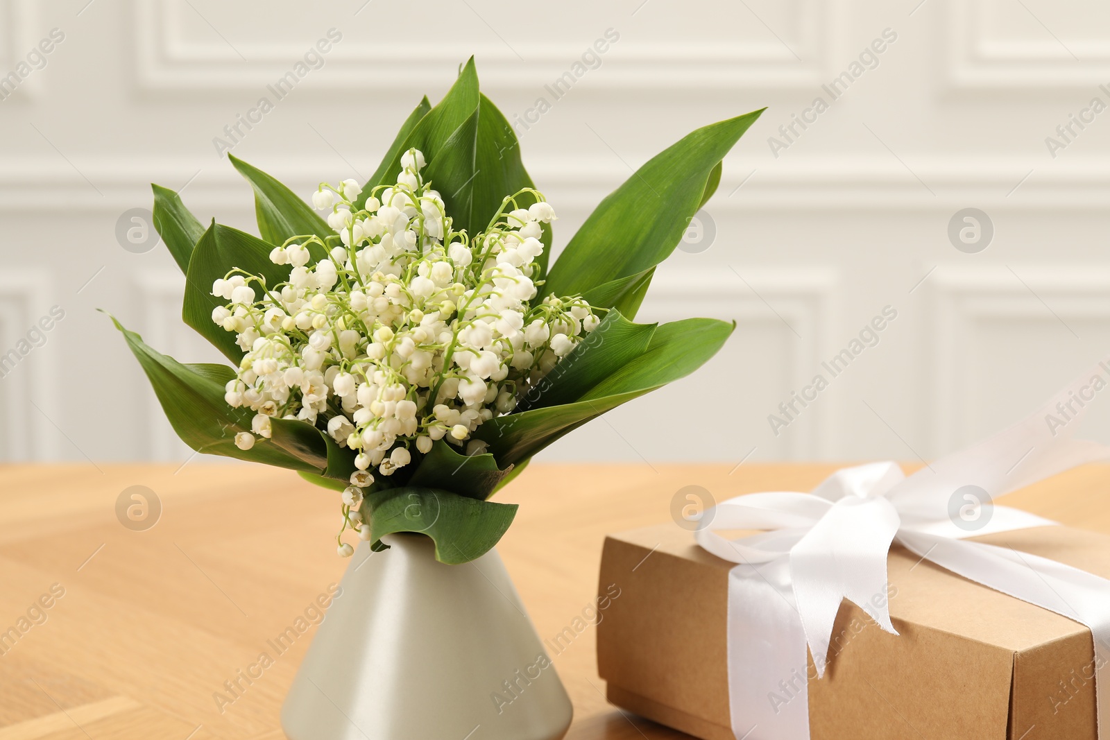 Beautiful lilies of the valley flowers and gift on wooden table, closeup Photo of Beautiful lilies of the valley flowers and gift on wooden table, closeup