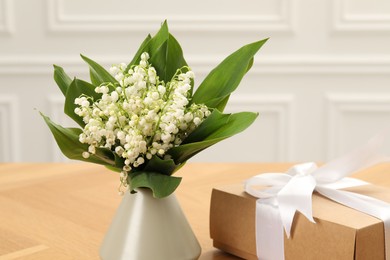 Photo of Beautiful lilies of the valley flowers and gift on wooden table, closeup