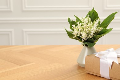 Photo of Beautiful lilies of the valley flowers and gift on wooden table. Space for text