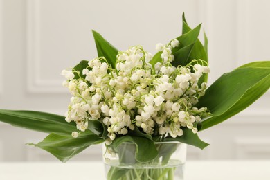 Photo of Beautiful lilies of the valley flowers in vase on white table, closeup
