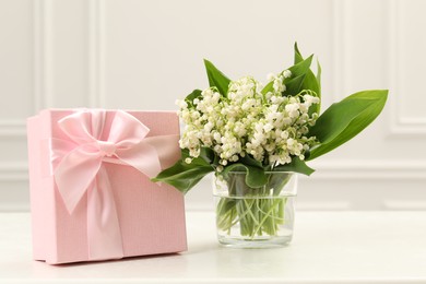 Photo of Beautiful lilies of the valley flowers and gift on white table