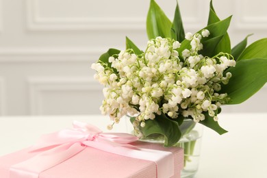 Photo of Beautiful lilies of the valley flowers and gift on white table, closeup