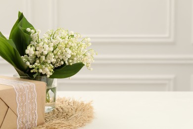 Photo of Beautiful lilies of the valley flowers and gift on white table. Space for text
