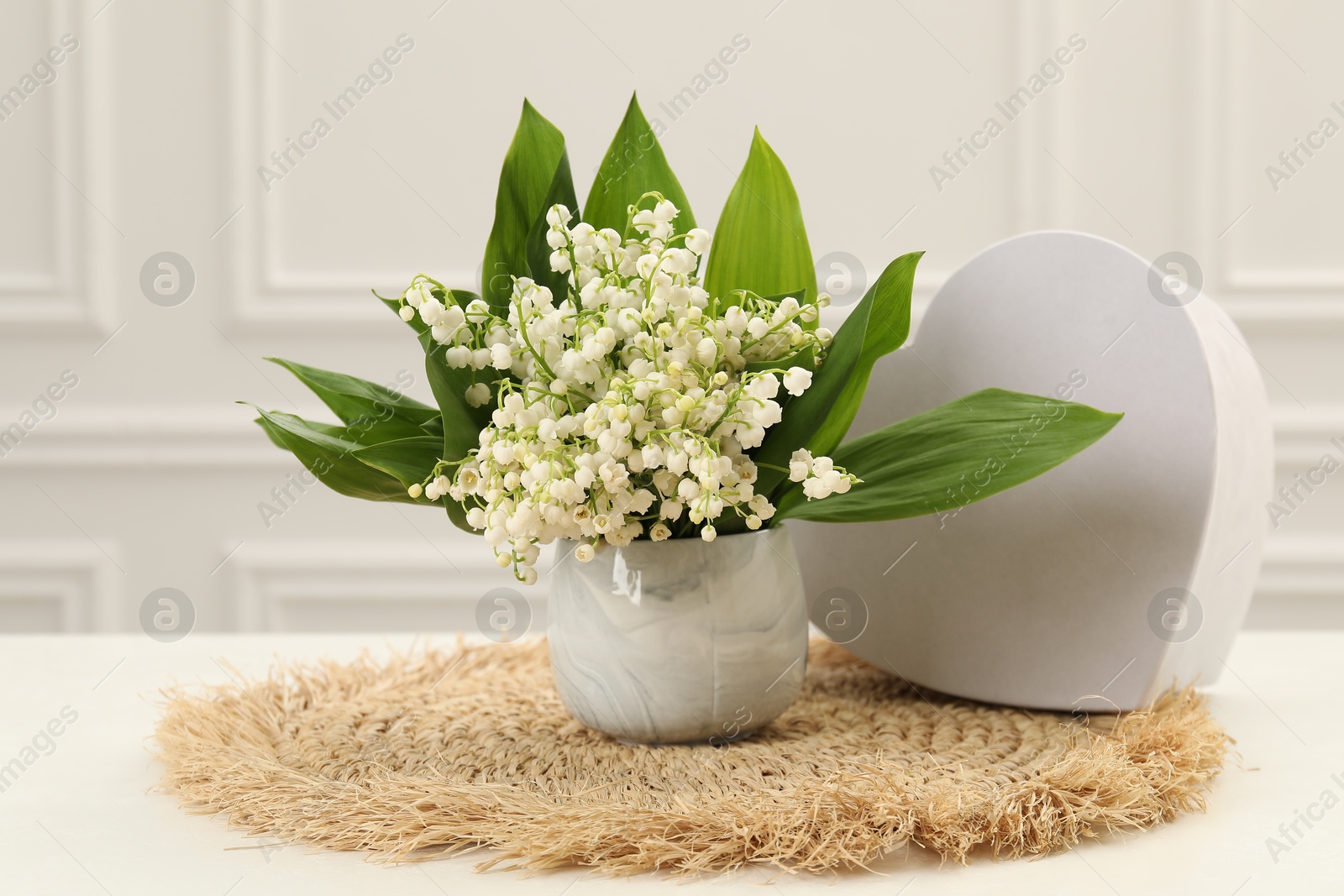 Beautiful lilies of the valley flowers and heart shaped gift box on white table Photo of Beautiful lilies of the valley flowers and heart shaped gift box on white table