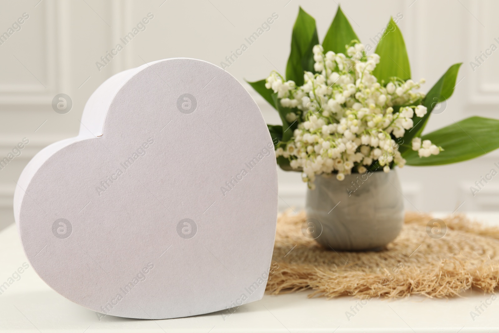 Beautiful lilies of the valley flowers and heart shaped gift box on white table Photo of Beautiful lilies of the valley flowers and heart shaped gift box on white table