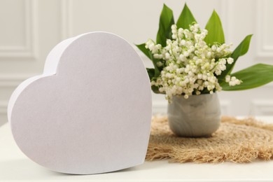 Photo of Beautiful lilies of the valley flowers and heart shaped gift box on white table