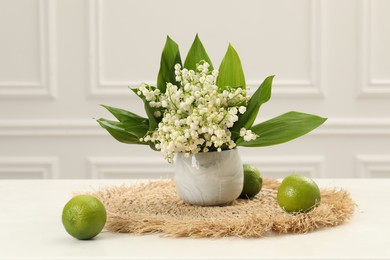 Photo of Beautiful lilies of the valley flowers in vase and limes on white table