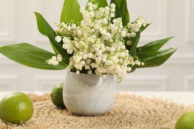 Photo of Beautiful lilies of the valley flowers in vase and limes on white table