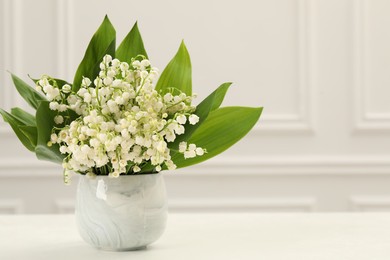 Photo of Beautiful lilies of the valley flowers in vase on white table. Space for text