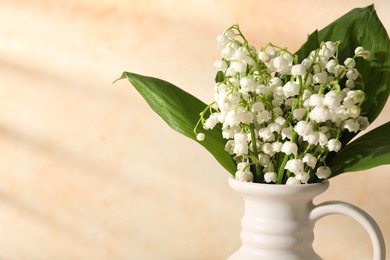 Photo of Beautiful lilies of the valley flowers in vase near beige wall, closeup. Space for text