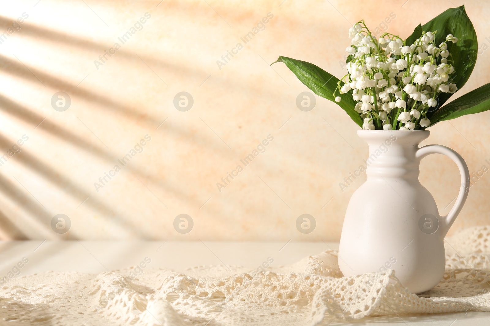 Beautiful lilies of the valley flowers in vase on white table near beige wall. Space for text Photo of Beautiful lilies of the valley flowers in vase on white table near beige wall. Space for text