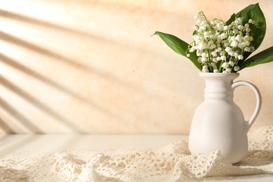 Photo of Beautiful lilies of the valley flowers in vase on white table near beige wall. Space for text