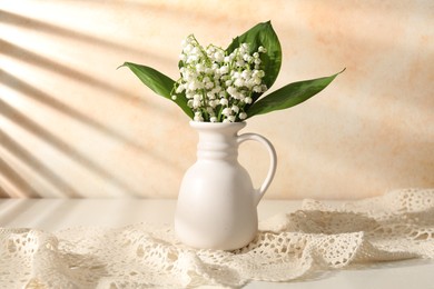 Photo of Beautiful lilies of the valley flowers in vase on white table near beige wall