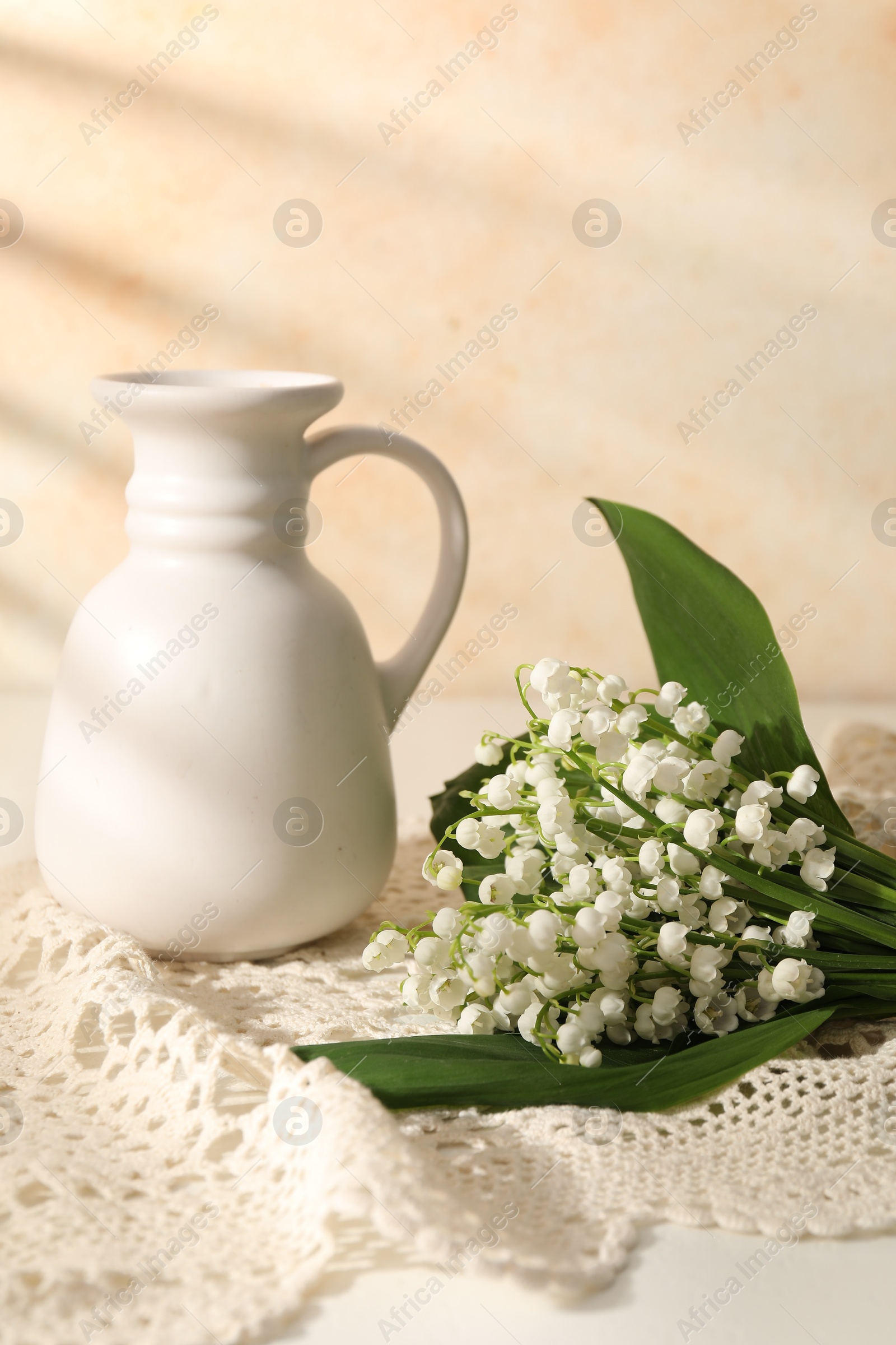 Beautiful lilies of the valley flowers and vase on white table near beige wall Photo of Beautiful lilies of the valley flowers and vase on white table near beige wall