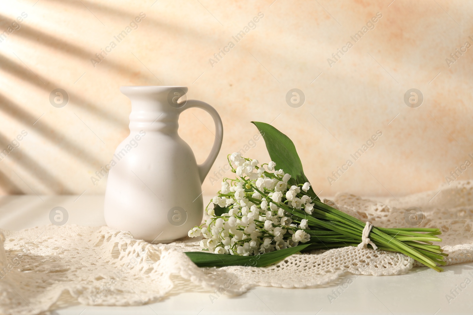 Beautiful lilies of the valley flowers and vase on white table near beige wall Photo of Beautiful lilies of the valley flowers and vase on white table near beige wall